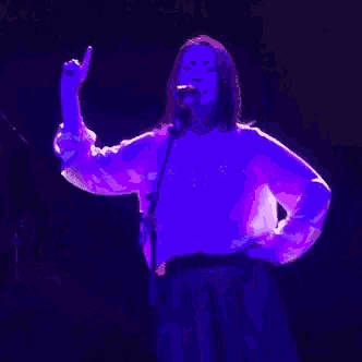 a woman singing into a microphone in a dark room with purple lights