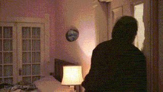 a man stands in a bedroom with a lamp and a clock on the wall