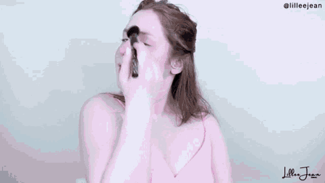 a woman is applying blush to her face with a brush .