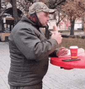 a man is sitting at a red table eating a hot dog and drinking coffee .