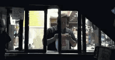 a man is standing in a drive thru window eating a hamburger .