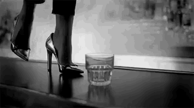 a woman wearing high heels is standing next to a glass of water .