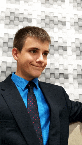 a young man in a suit and tie stands in front of a wall