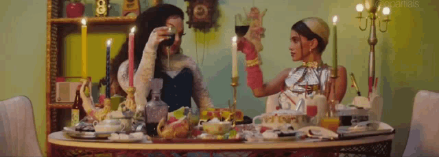 two women are sitting at a table with candles toasting with wine glasses .