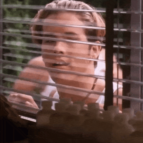 a woman is looking out of a window with blinds on it