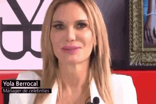 a woman in a white jacket is talking into a microphone while standing in front of a picture frame .