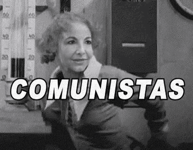 a black and white photo of a woman sitting at a table with the word comunistas written in white letters .