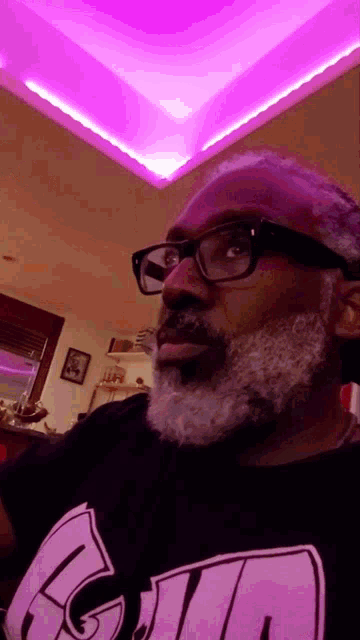 a man with glasses and a beard is wearing a black shirt that says ' a ' on it