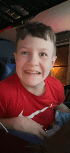 a young boy wearing a red nike shirt looks at the camera