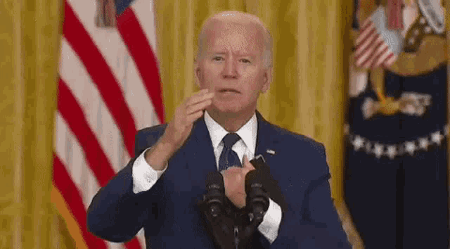 a man in a suit and tie is giving a speech in front of a microphone in front of an american flag .