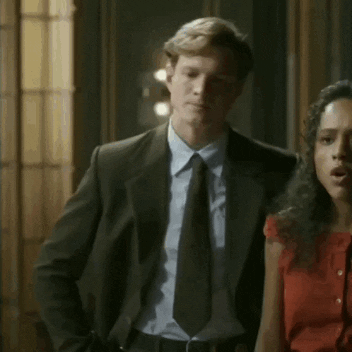 a man in a suit and tie stands next to a woman in a red dress