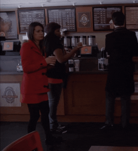 a woman in a red coat is standing in front of a counter with a sign that says ' coffee shop ' on it