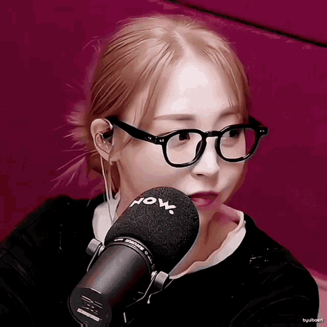 a woman wearing glasses and earbuds is talking into a shure microphone