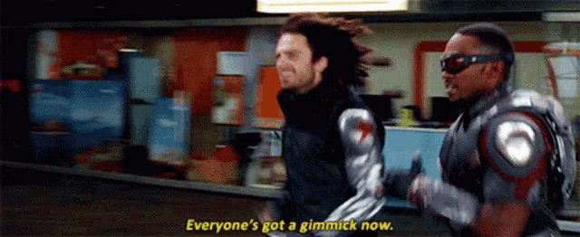 two men in superhero costumes are running and one of them is saying everyone 's got a gimick now .