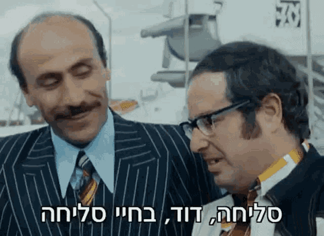 two men in suits and ties are standing next to each other and one of them has a foreign language written on his shirt .
