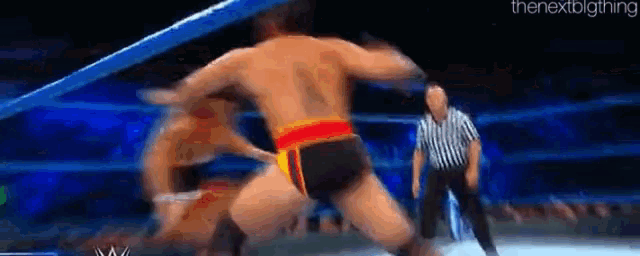 a man is wrestling another man in a wrestling ring while a referee looks on .