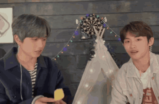 two boys are sitting in front of a dart board and a teepee .