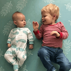 two babies are laying on a blanket and one is wearing a whale outfit