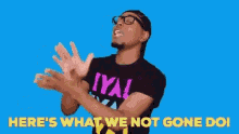 a man wearing a iya t-shirt is clapping his hands in front of a blue background