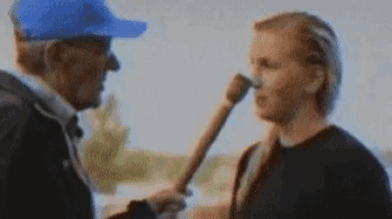 a man in a blue hat is talking to another man while holding a bat .