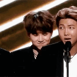 two men are standing next to each other in front of a microphone and one of them is making a funny face .