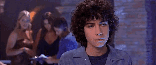 a man with curly hair is standing in front of a group of women in a club .