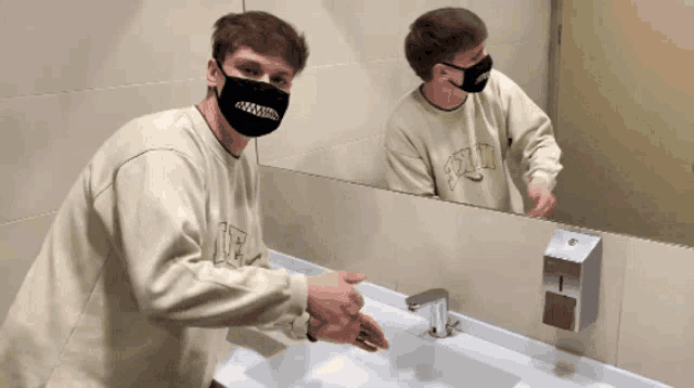 a man wearing a mask is washing his hands in front of a mirror