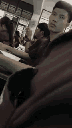 a man is sitting at a desk in a classroom with other students .