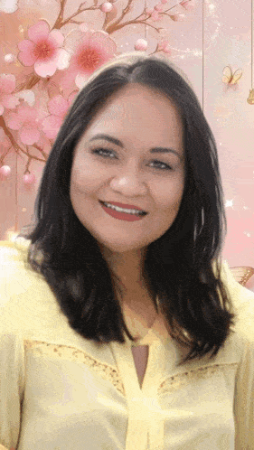 a woman in a yellow shirt is smiling in front of a pink background with flowers