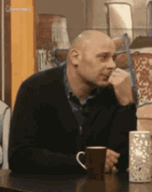 a man is sitting at a table with a cup of coffee and a candle .