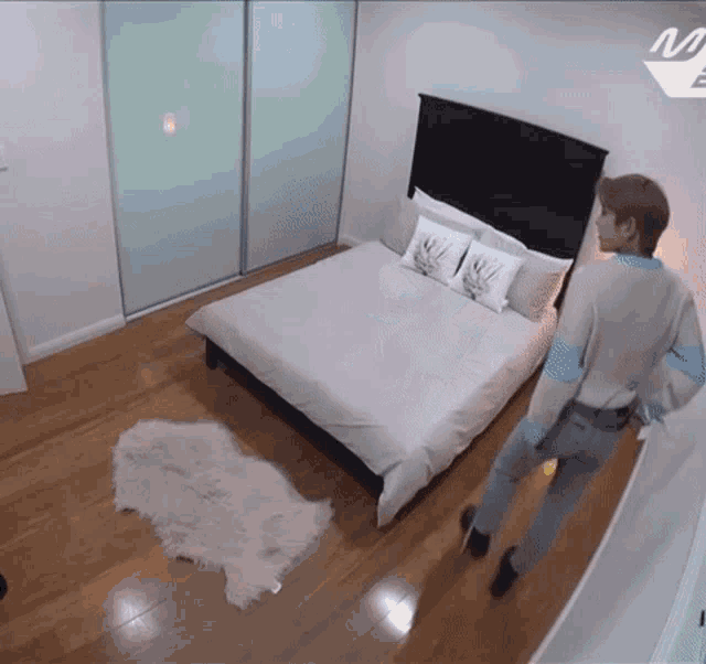 a man in a sweater stands in a bedroom with a bed and a rug
