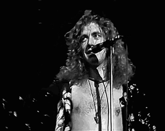 a black and white photo of a man singing into a microphone on stage .