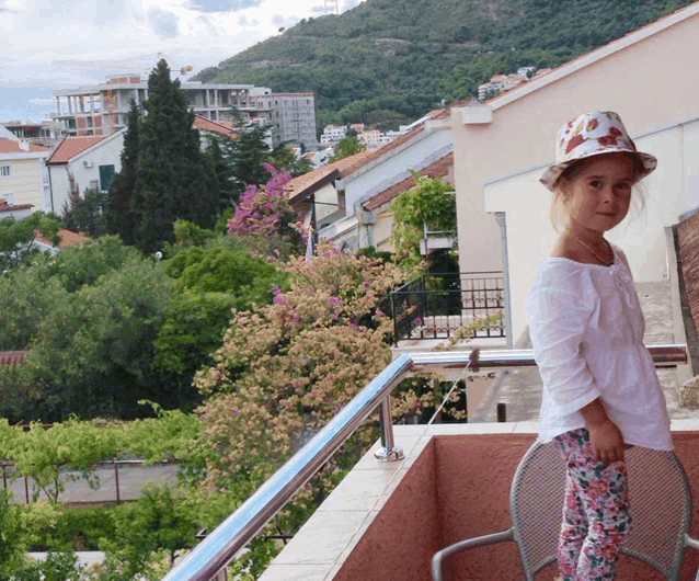 a little girl wearing a hat is standing on a balcony overlooking a city