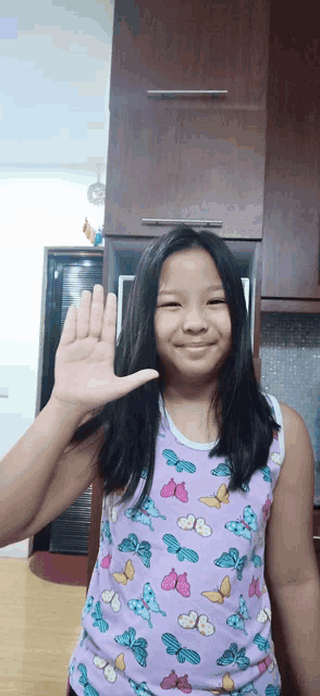 a girl wearing a purple tank top with butterflies on it waves her hand