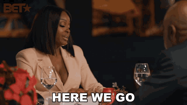 a woman is sitting at a table with a man and says here we go