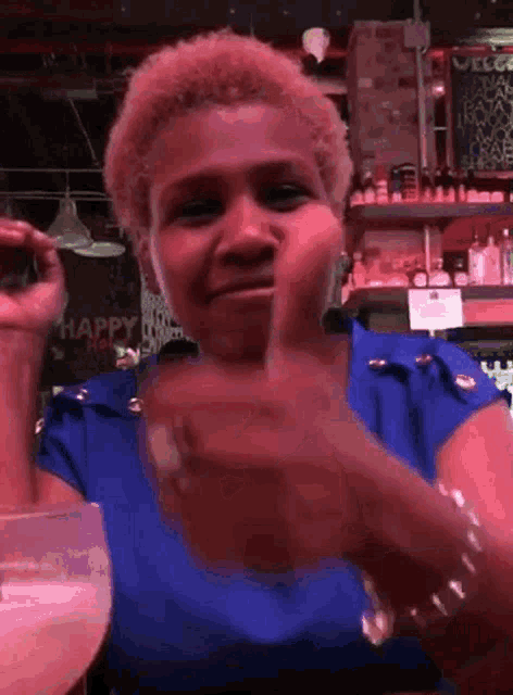a woman in a blue shirt is giving a thumbs up in front of a sign that says happy