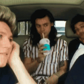 a man is drinking through a straw from a cup while sitting in a car .