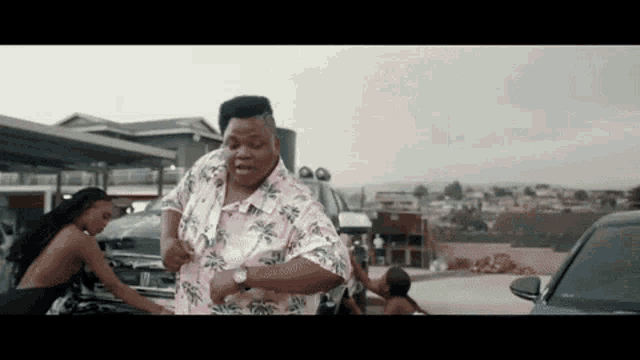 a man in a pink shirt is dancing in a parking lot while a woman holds his shirt .