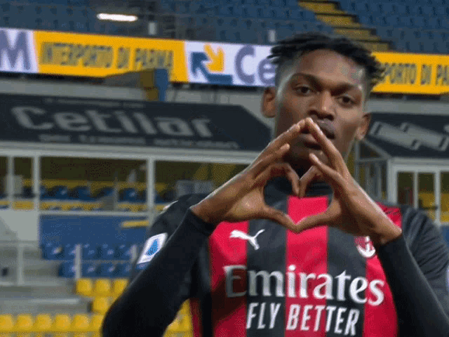 a man wearing a emirates fly better shirt makes a heart shape with his hands