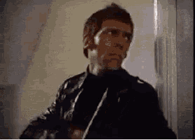 a man in a leather jacket is standing in a doorway holding a gun .