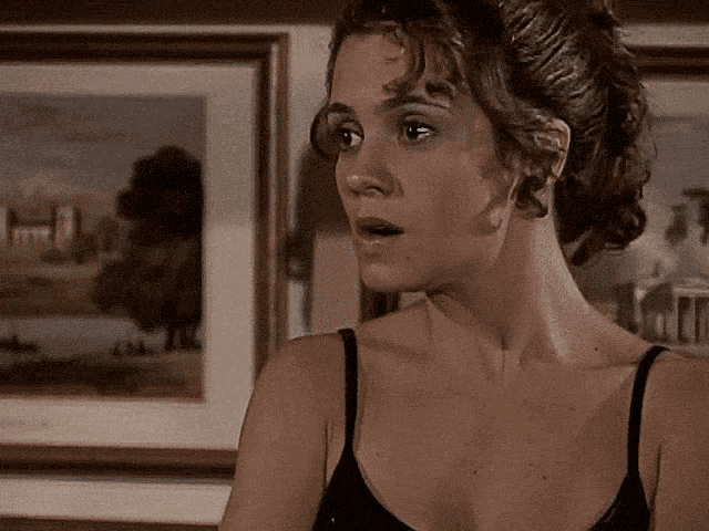 a woman in a black tank top is standing in front of a framed painting