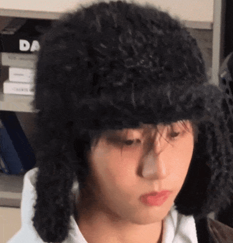 a young man wearing a black hat with ear flaps is looking down .