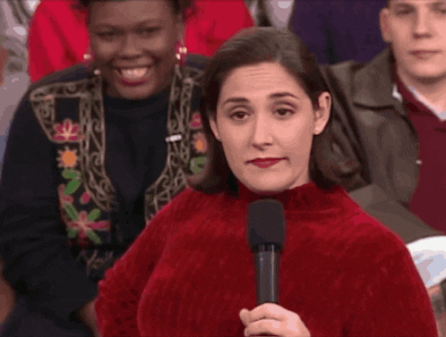 a woman in a red sweater holds a microphone in front of a crowd of people