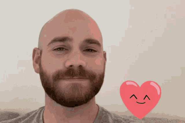 a man with a beard is smiling in front of a pink heart with a face drawn on it
