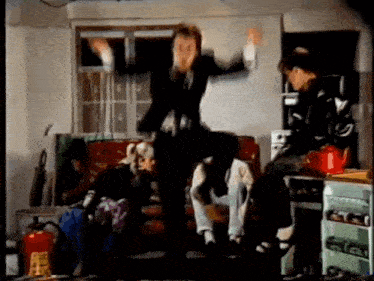 a group of people are dancing in a living room with a red fire extinguisher in the background .