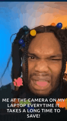 a man with dreadlocks is making a funny face while taking a picture of himself with a camera on his laptop .