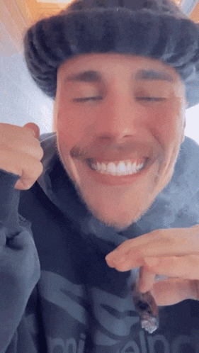 a man wearing a hat and a hoodie with the word adidas on it is smoking a cigarette