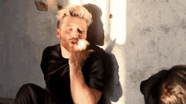 a man with blonde hair and a beard is sitting down and blowing a kiss