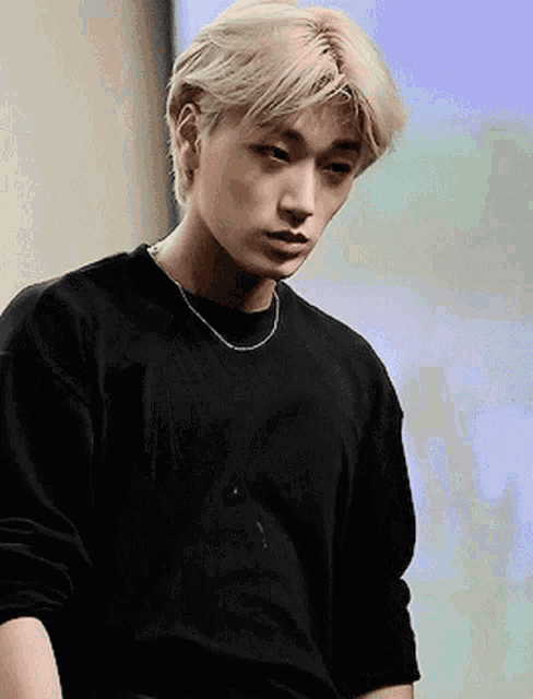 a young man with blonde hair is wearing a black sweater and a necklace .