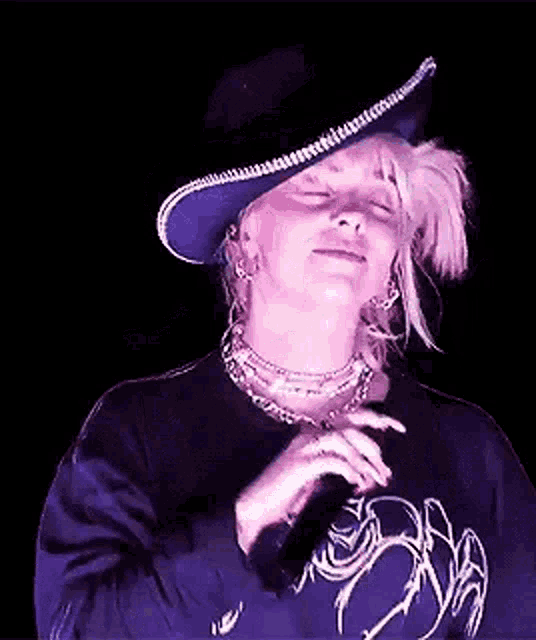 billie eilish is wearing a cowboy hat and singing into a microphone on stage .